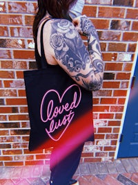 a woman wearing a black tote bag with the words loved us on it